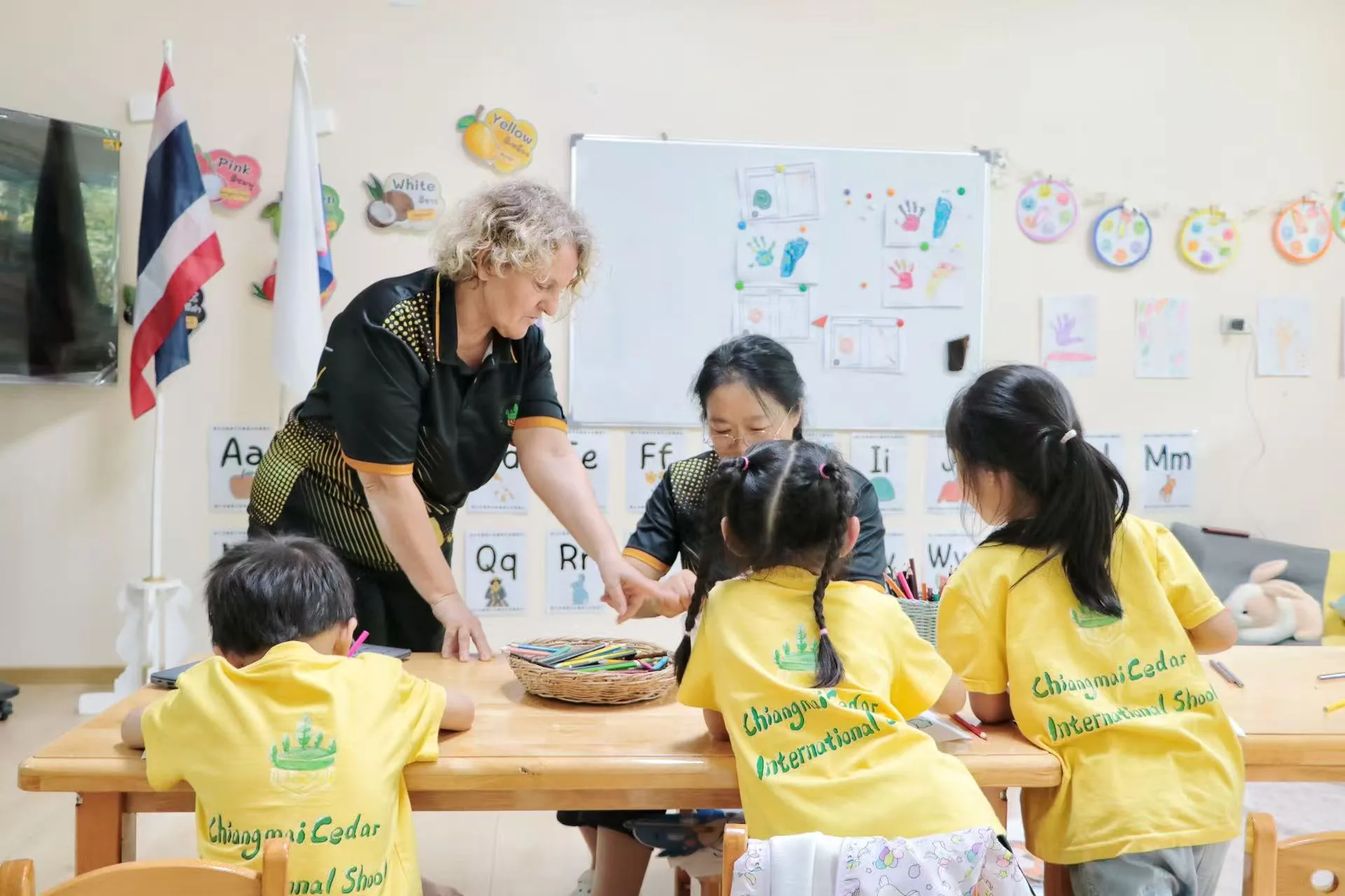Two teachers guiding young students through letters and hands-on craft